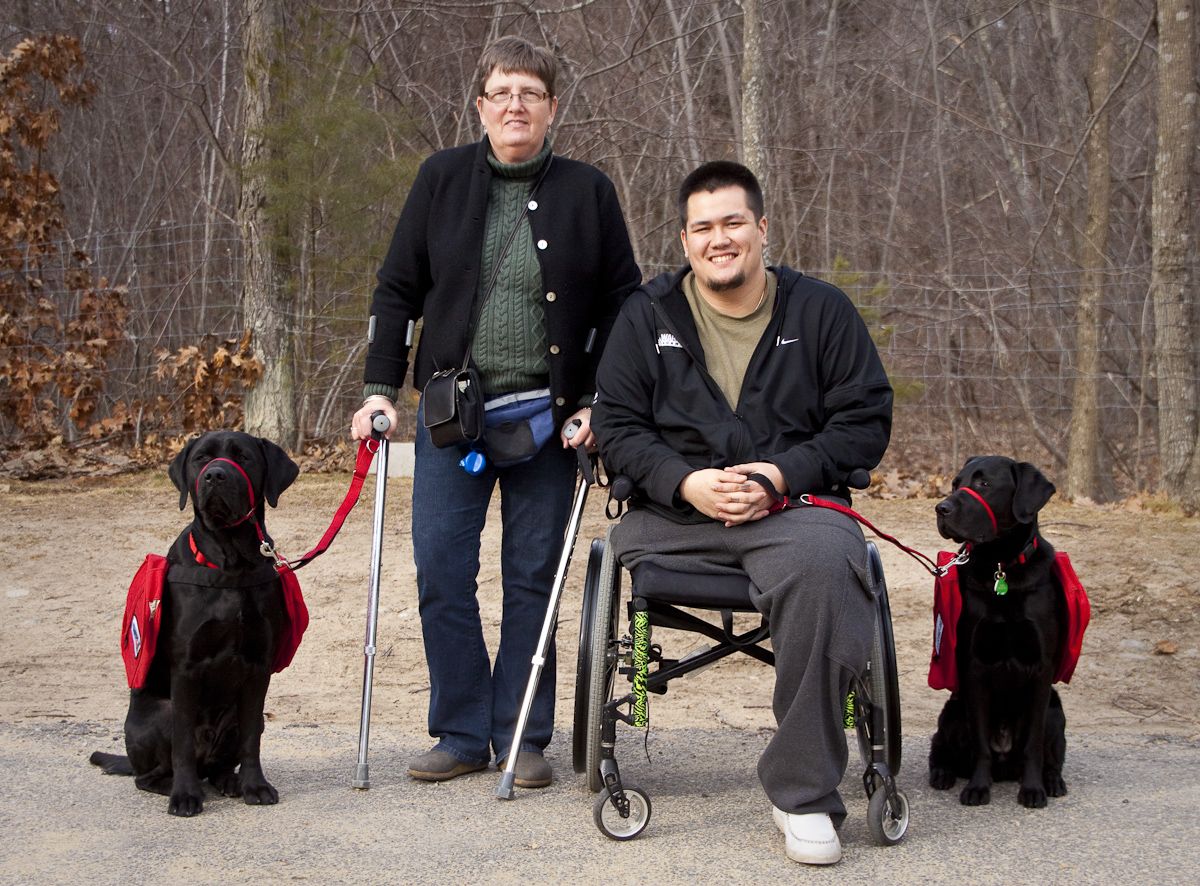 Man with one leg in wheelchair, woman on crutches, two labradore service dogs